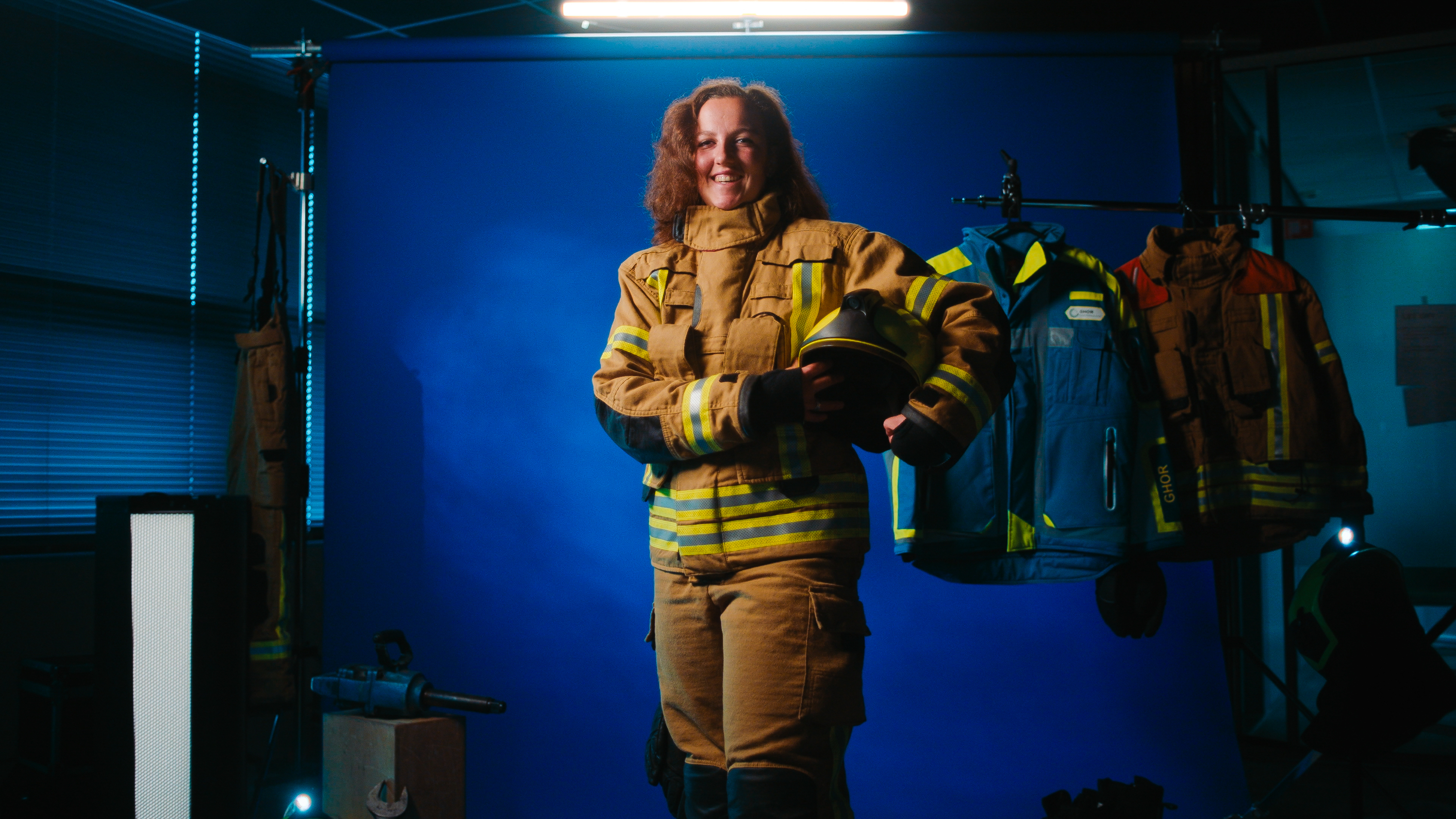 Lachende vrouw in brandweerpak met brandweerhelm onder haar arm