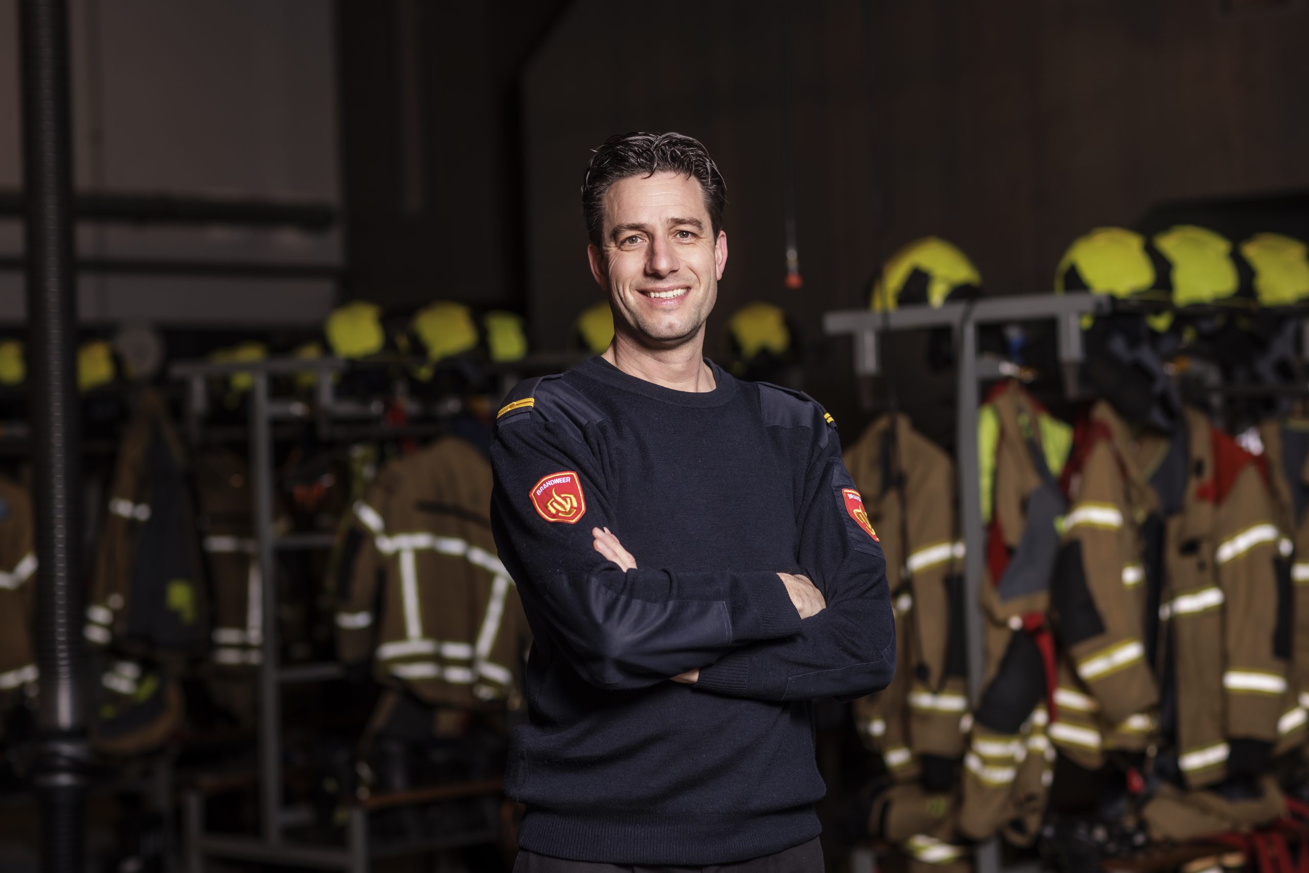 Man in brandweer tenue met over elkaar geslagen armen lachend kijkend in de camera