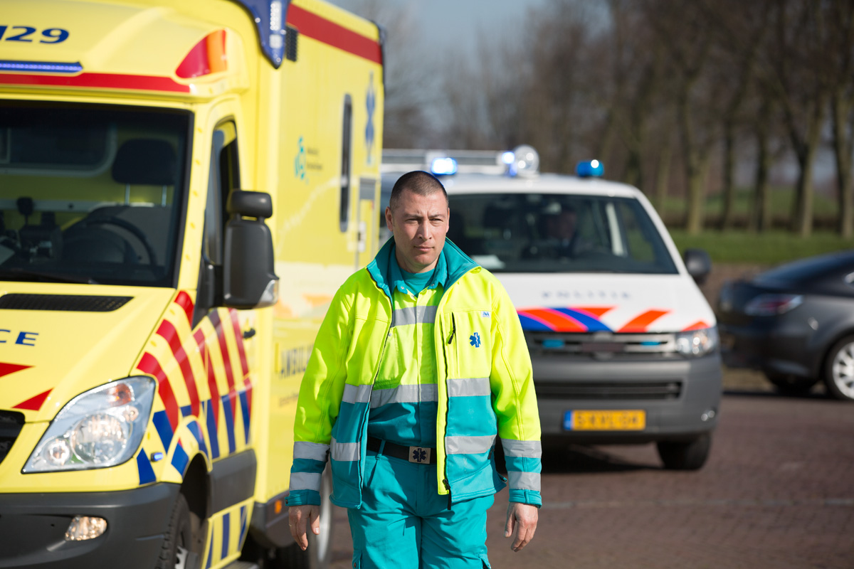 Ambulancemedewerker naast ambulance en voor politieauto