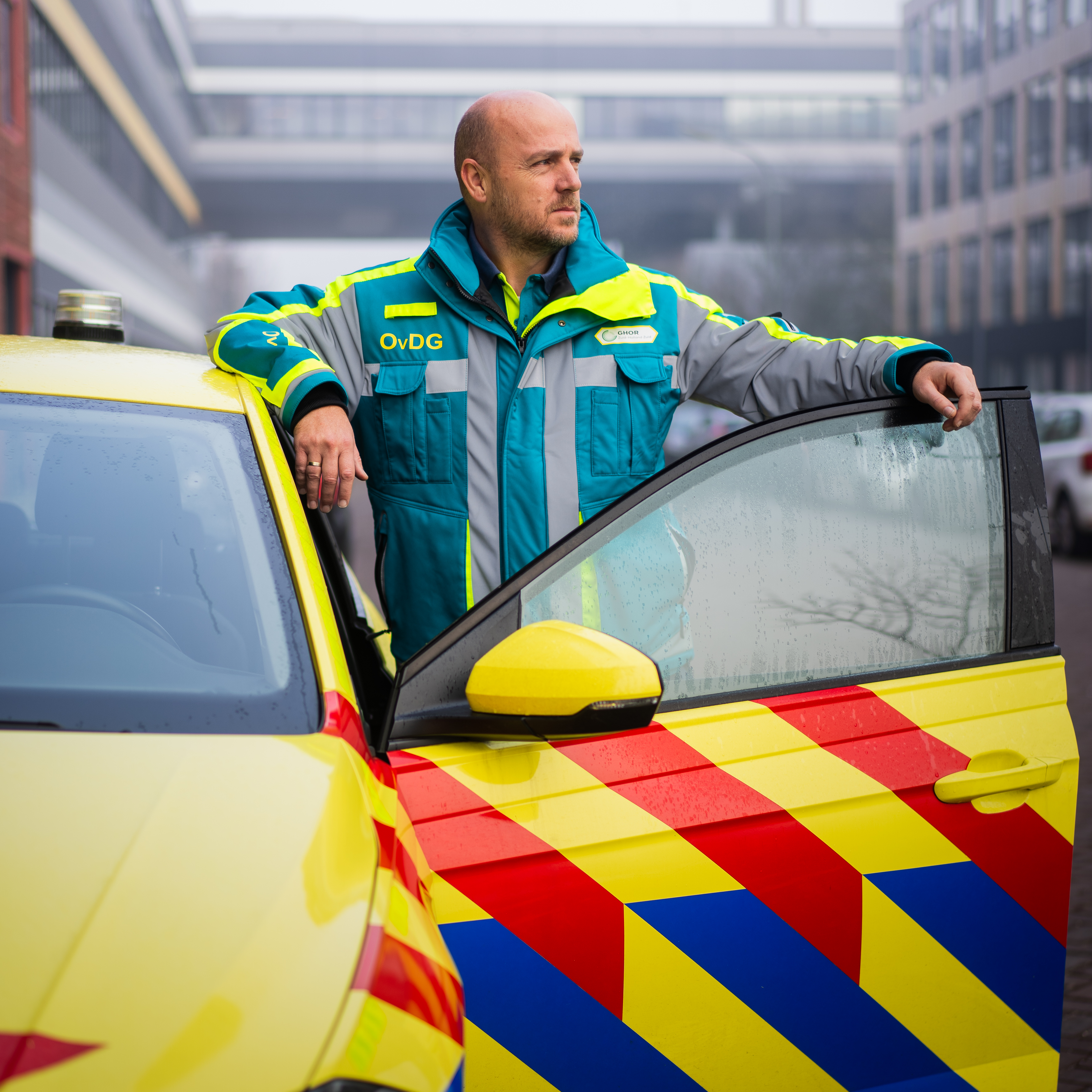 Sander tussen opengeslagen autodeur in de verte turend