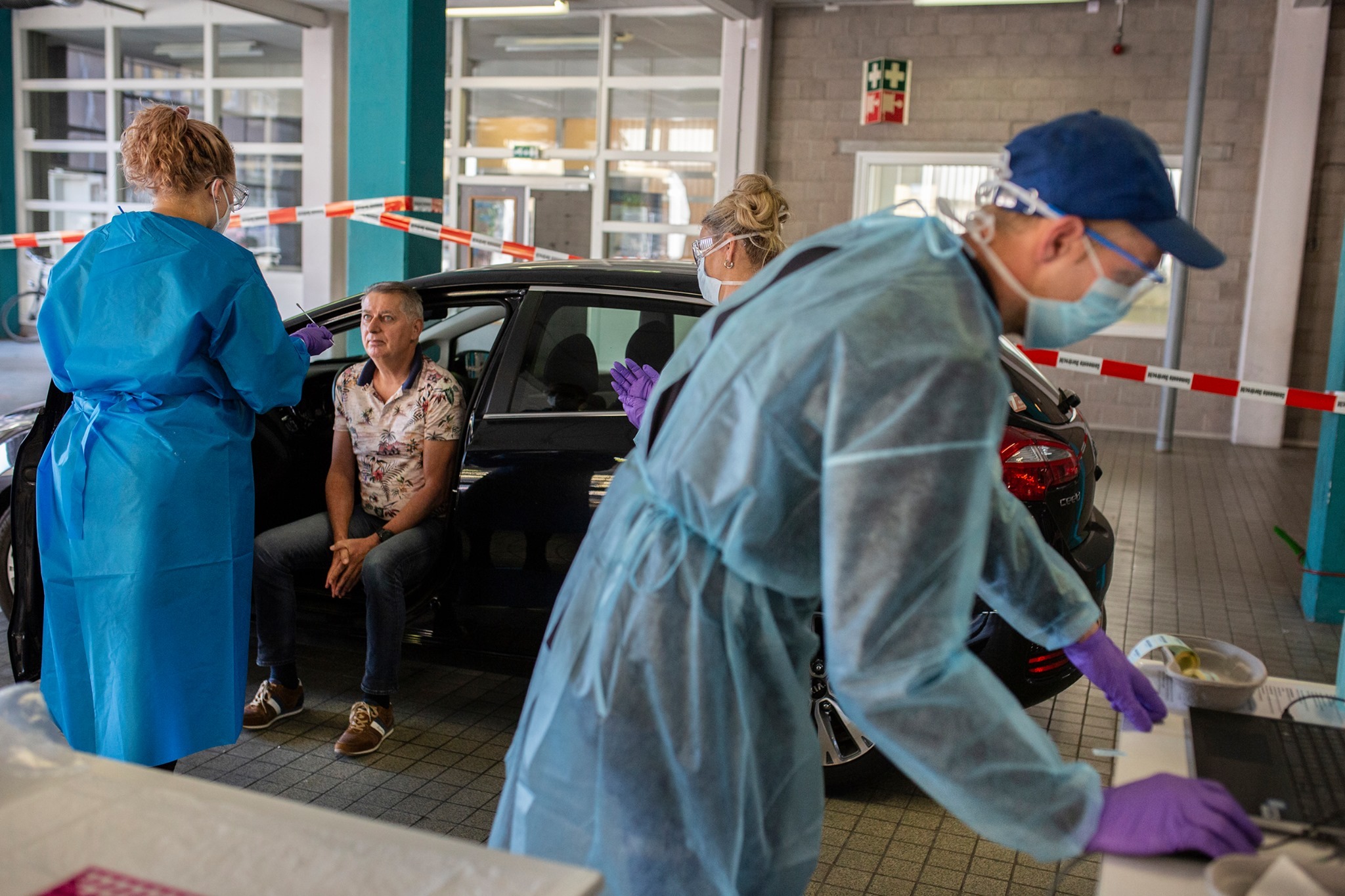 Man ondergaat coronatest in teststraat waar 3 GGD-medewerkers aanwezig zijn