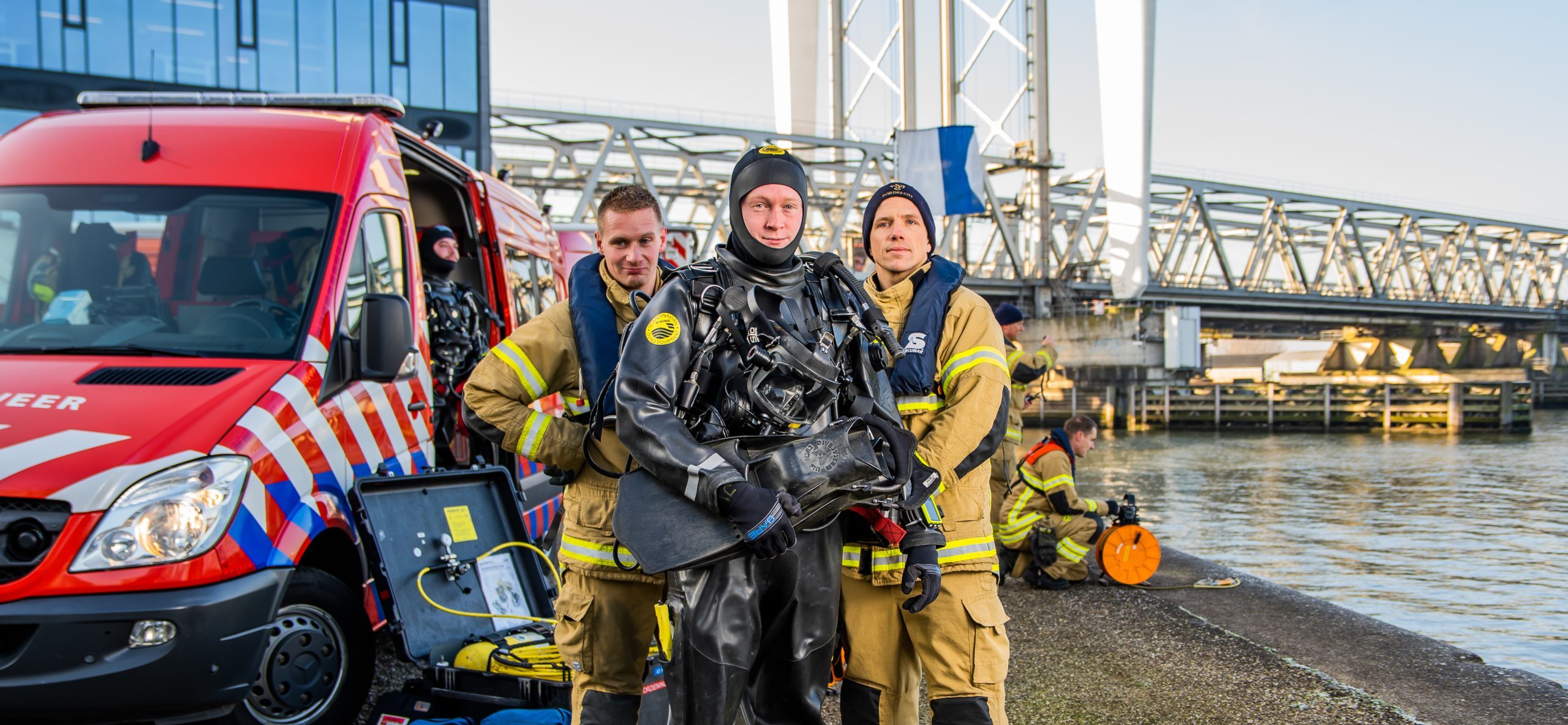 Foto van brandweerduiker in duikpak en brandweermensen aan de waterkant in Dordrecht