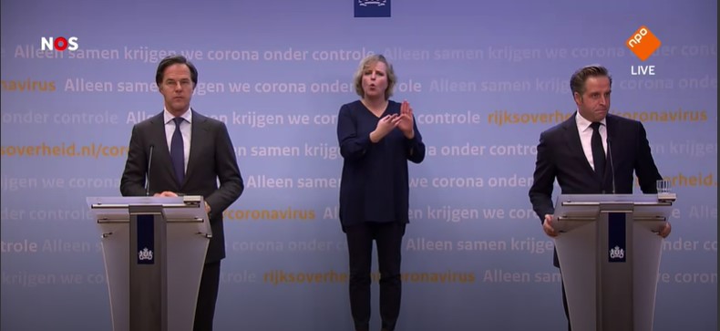 Een gebarentolk beeld de woorden van Mark Rutte en Hugo de Jonge uit tijdens een persconferentie