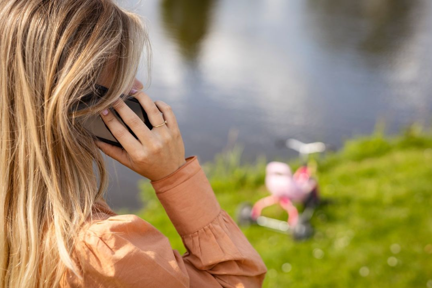Jonge vrouw met smartphone aan haar oor, in de verte ligt een kinderfiets langs het water