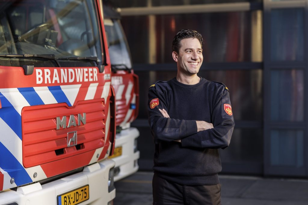Marc staat lachend met zijn handen over elkaar voor brandweerwagen
